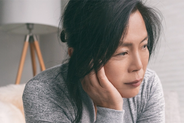 Adrenal-Fatigue-Doctor A middle-aged asian woman sitting on her couch, resting her head on her hand, suffering from adrenal fatigue. Get treatment for adrenal fatigue syndrome from Tanya Zboril, NP of TBT Medical in Halifax.