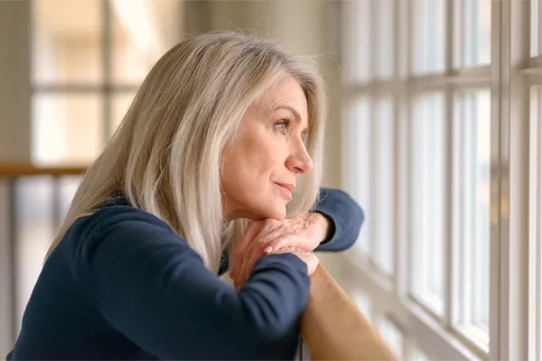 Adrenal-Hormone-Disorder-Clinic A mature woman in a blue shirt looks out the window with melancholy. Schedule treatment for adrenal hormone disorder from Tanya Zboril, NP of TBT Medical in Halifax.
