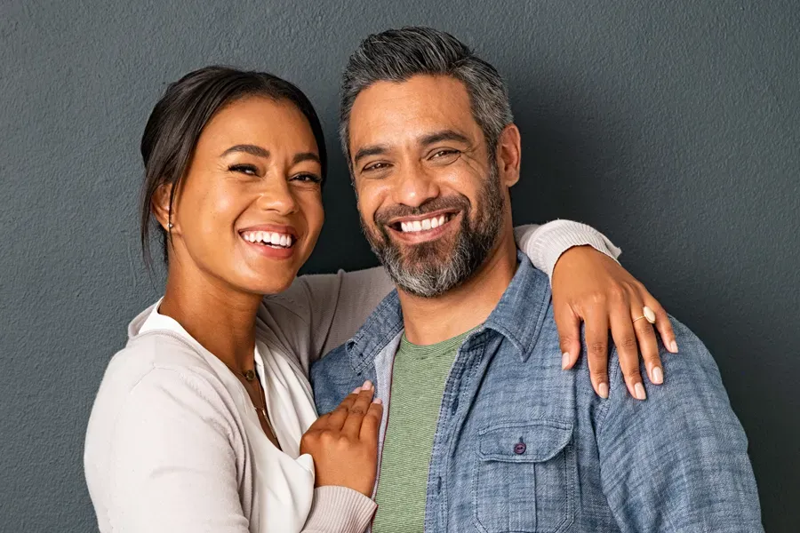 Bioidentical-Hormone-Therapy-Doctor A middle-aged couple with their arms around each other standing against a gray background and smiling, happy with the bioidentical hormone therapy they received from Tanya Zboril, NP of TBT Medical in Halifax.