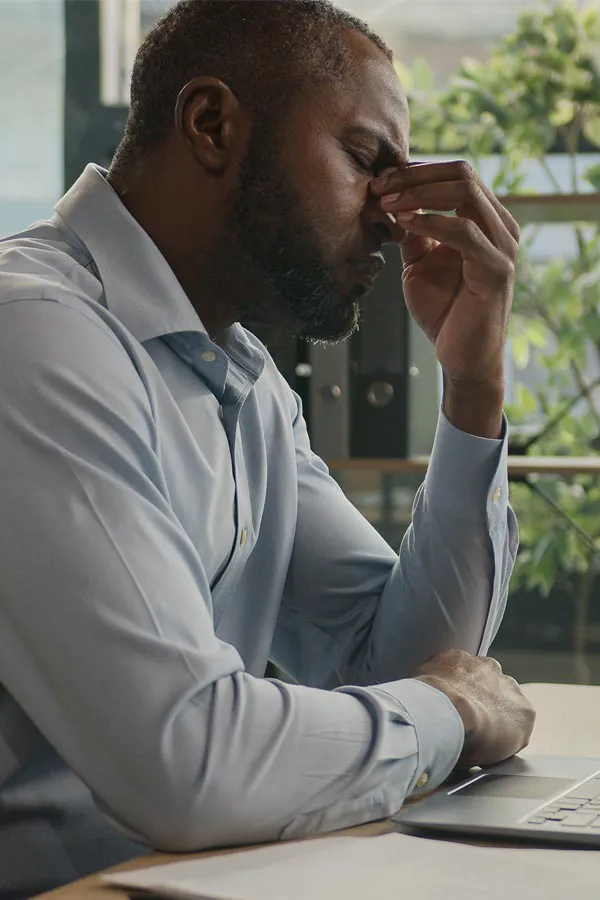 Chronic-Fatigue-Treatment A black man rubbing the top of his nose at his desk, in need of chronic fatigue treatment from Tanya Zboril, NP of TBT Medical in Halifax.