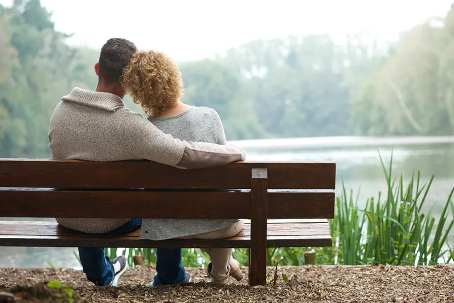 Functional-Medicine-Doctor A couple wearing sweaters seen from behind sitting on a bench and looking out at a relaxing lake and forest, representing functional medicine treatment from Tanya Zboril, NP of TBT Medical in Halifax.