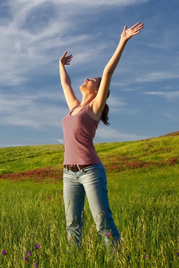 Graves-Disease-Treatment A woman in a tank top and jeans looks up with her arms outstretched to the sky in a field after successful treatment for Grave's Disease from Tanya Zboril, NP of TBT Medical in Halifax.