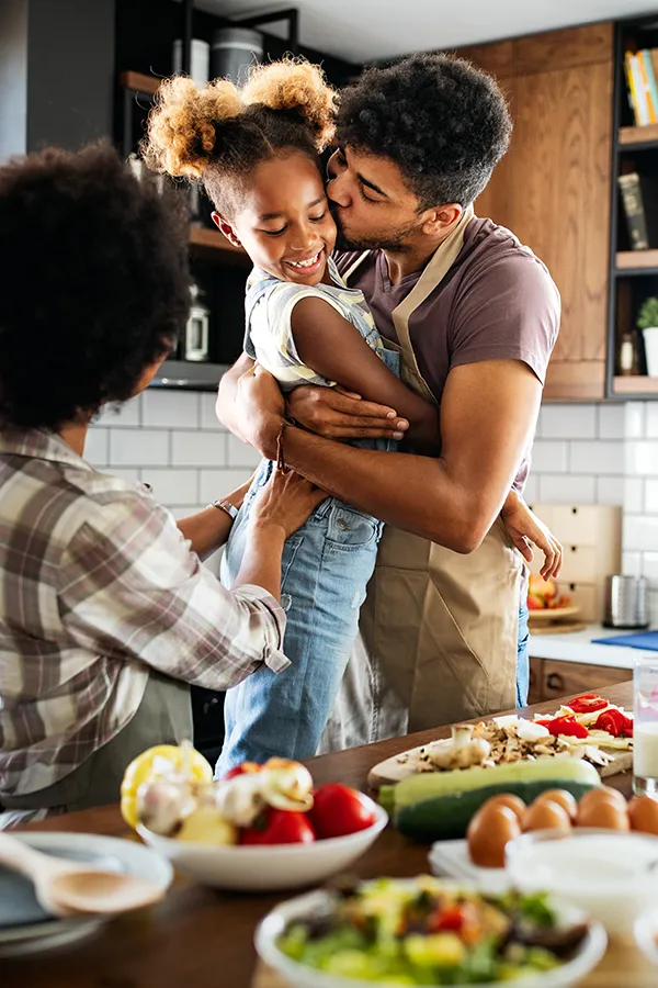 Gut-Health-Treatment A man holds his daughter and kisses her cheek as the family makes a healthy dinner in the kitchen. Get help for digestive issues and gut health from Tanya Zboril, NP of TBT Medical in Halifax.
