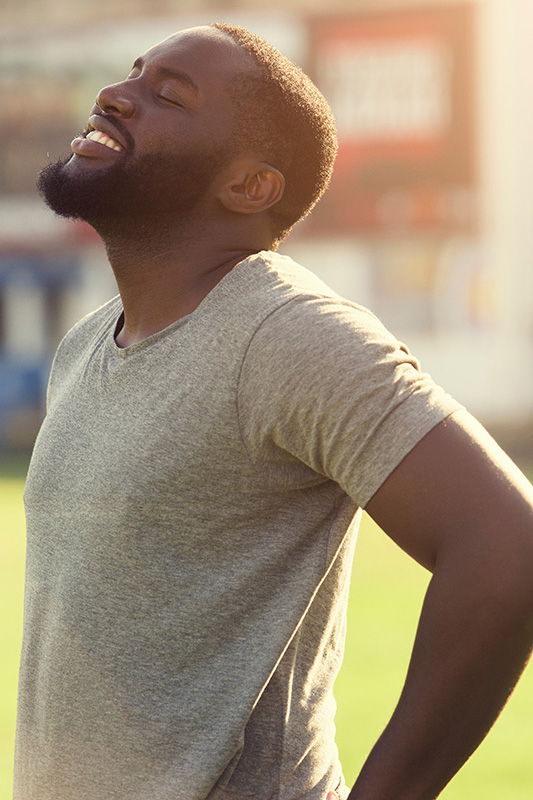 Lean-Muscle-and-Recovery-Treatment A black man in a gray t-shirt and smiles, looking up with closed eyes after a satisfying workout. Get treatment for lean muscle loss and recovery from Tanya Zboril, NP of TBT Medical in Halifax.
