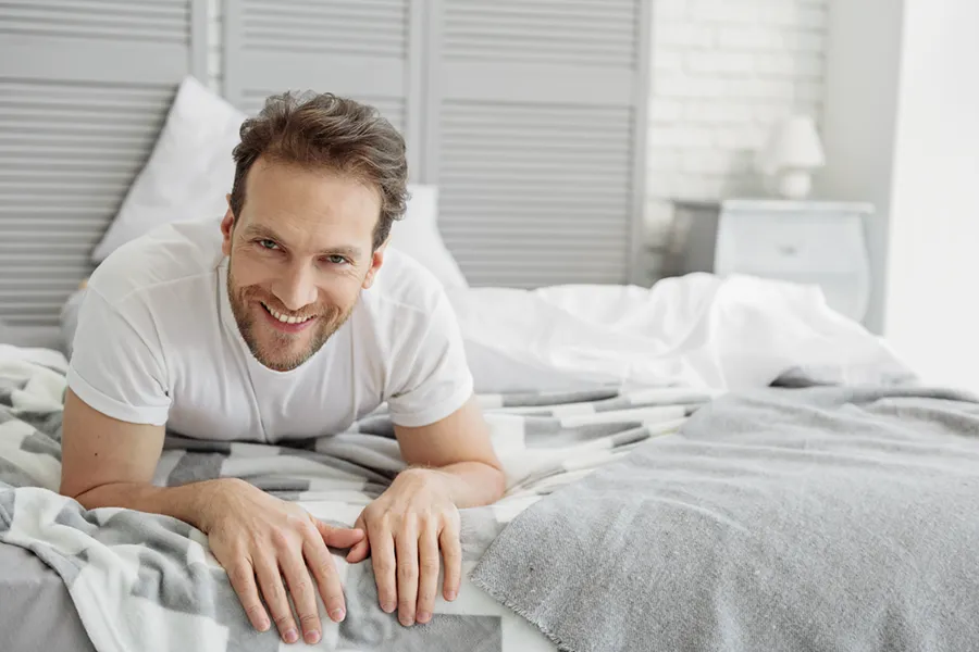 Low-Libido-in-Men-Doctor A dirty-blonde haired man lays on his stomach in bed smiling. Schedule treatment for low libido in men from Tanya Zboril, NP of TBT Medical in Halifax.