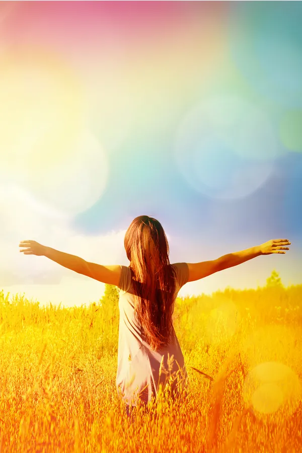 Ottawa-NAD-Therapy-Treatment Woman standing in a golden field with arms outstretched toward a vibrant, rainbow-hued sky, symbolizing vitality and inner renewal with NAD Therapy offered by Tanya Zboril, NP of TBT Medical in Halifax.