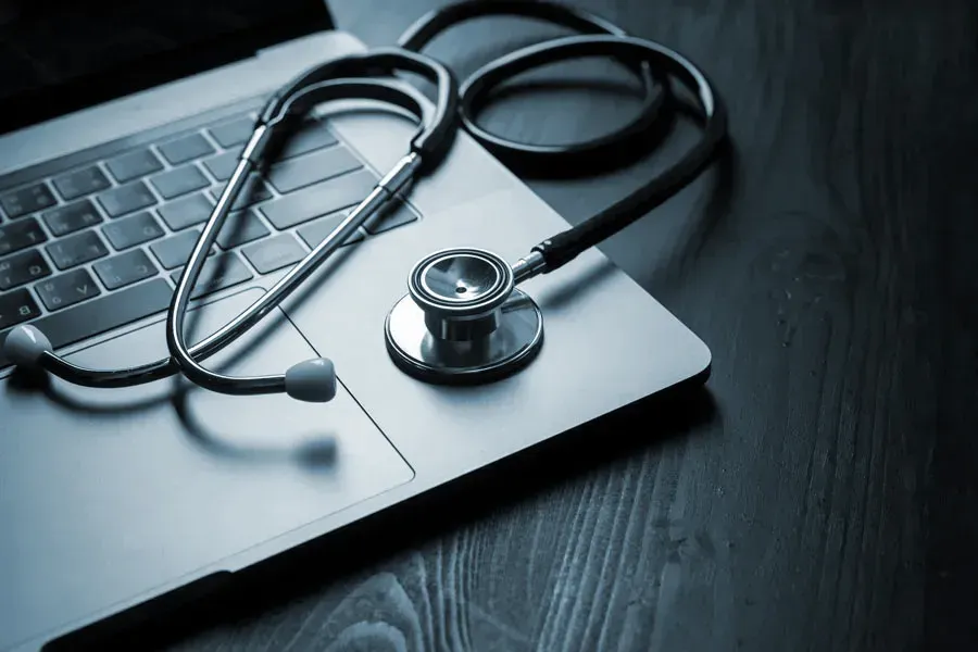 Telemedicine-Doctor An open laptop with a stethoscope lying on it on a wooden table, symbolizing telemedicine care from Tanya Zboril, NP of TBT Medical in Halifax.
